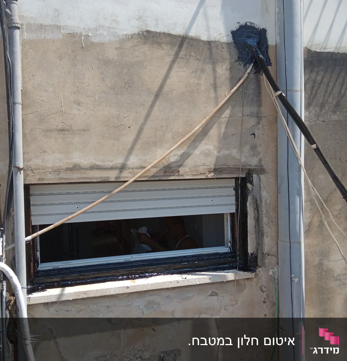 איטום חלון עם חומר שחור על קיר חיצוני